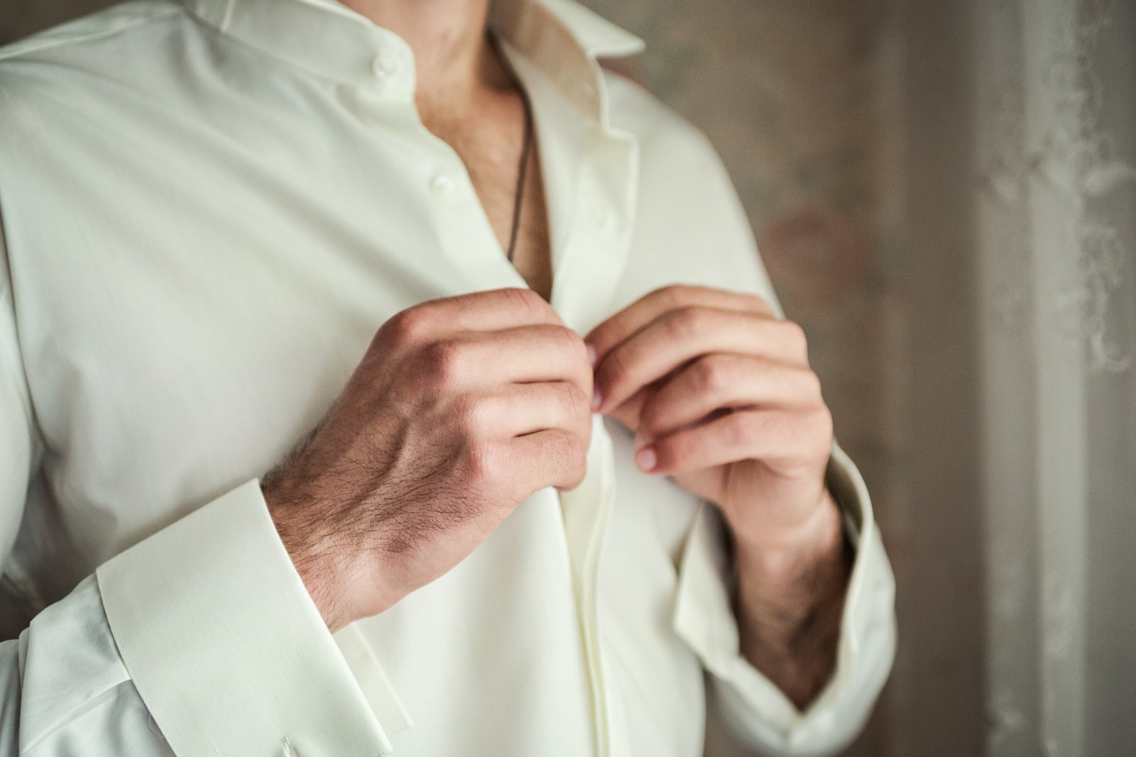 Close-up of a man's hands buttoning a shirt, a task cervical myelopathy can make difficult