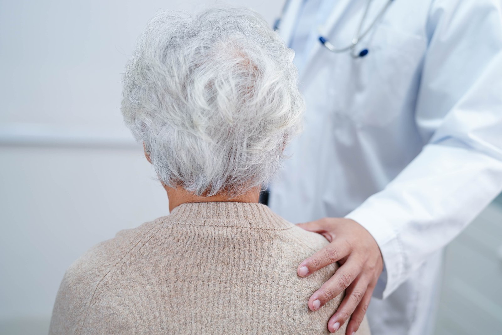 A doctor rests a reassuring hand on the shoulder of an older woman with white hair