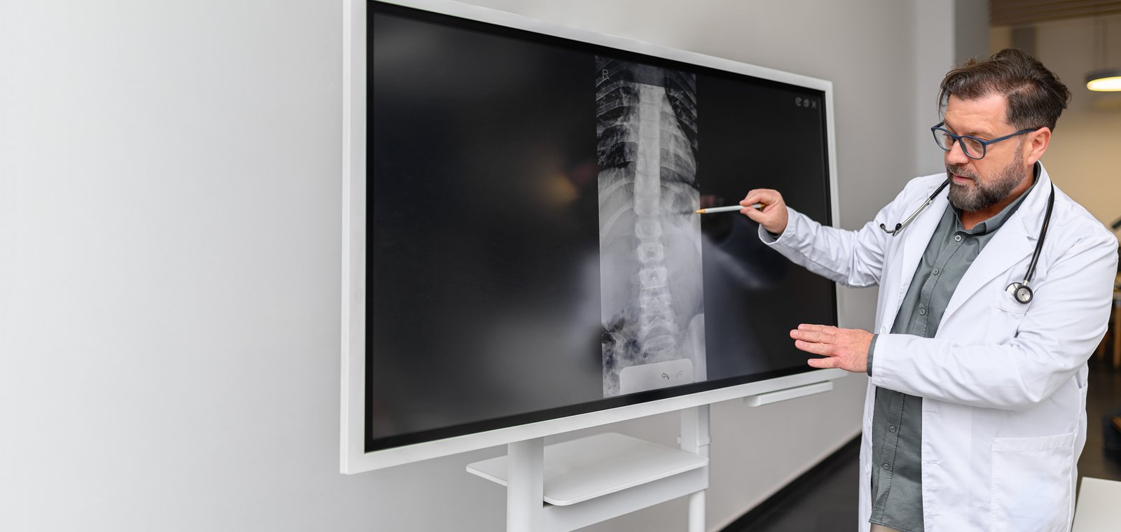 A doctor pointing to a lumbar spine X-ray on a large screen