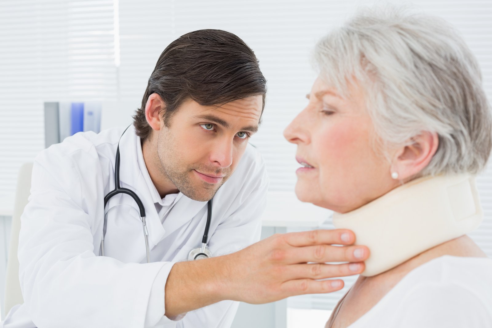 A doctor examining the neck of an older woman wearing a cervical collar